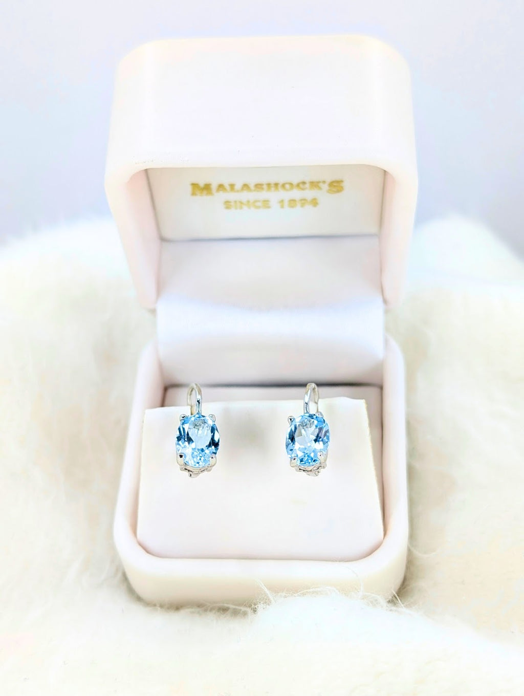 Pair of blue gemstone earrings in a Malashock's jewelry box on a white fur surface.
