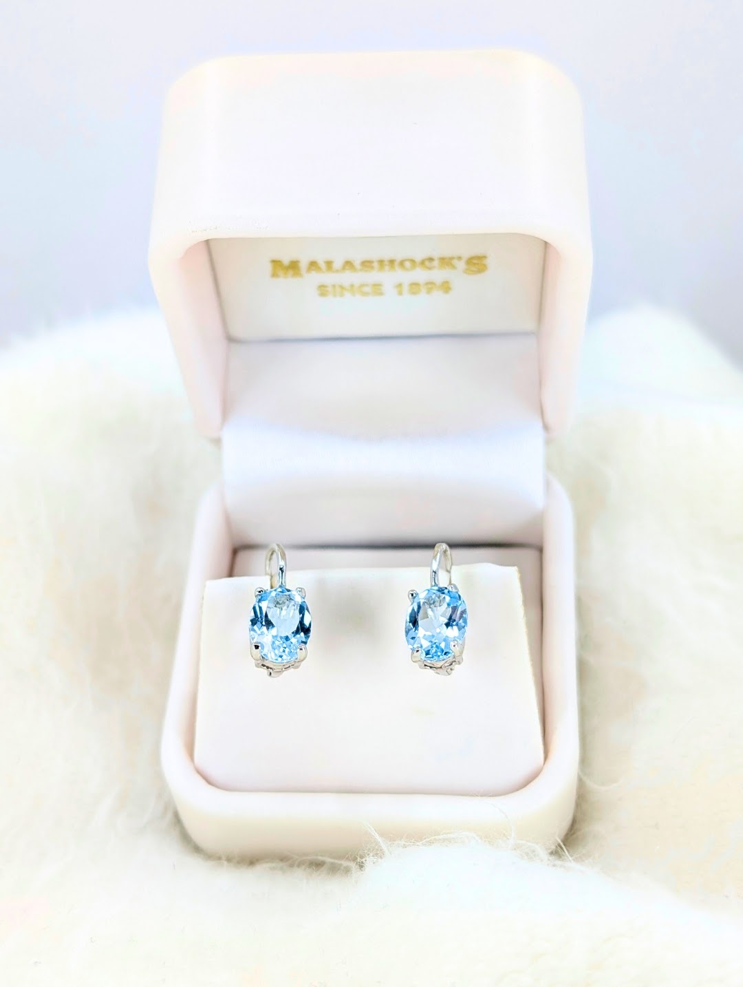 Pair of blue gemstone earrings in a Malashock's jewelry box on a white fur surface.