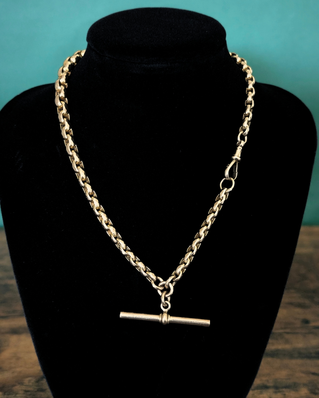 Gold Albert watch chain necklace with a dog clip on a black bust against a teal background