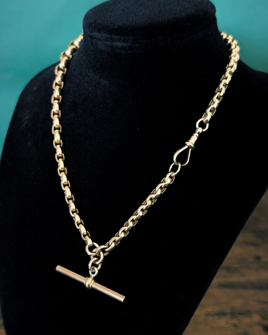 Antique yellow gold belcher Albert chain with a swivel clasp on a black bust against a teal background