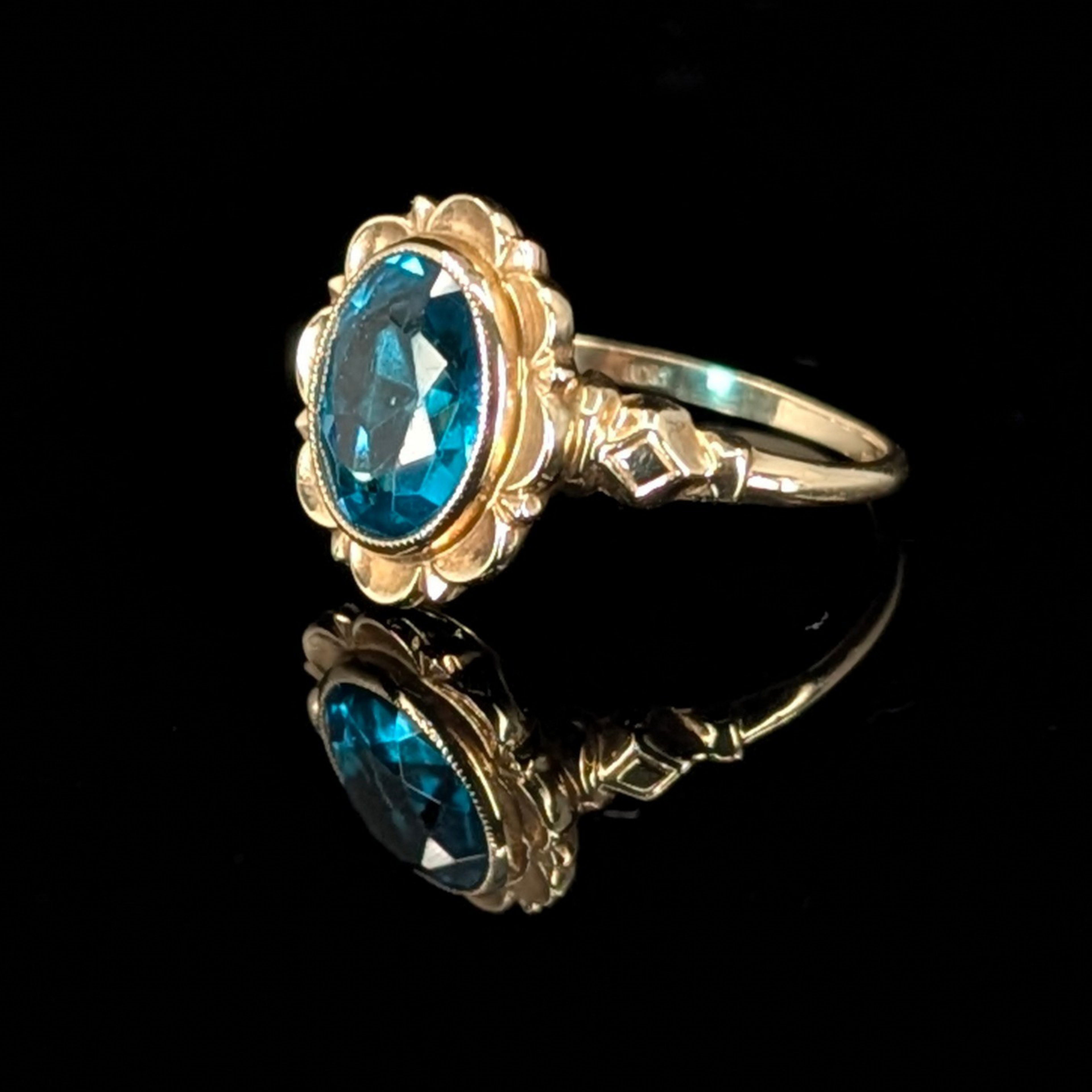 Art deco style gold engagement ring with a blue gemstone on a black background