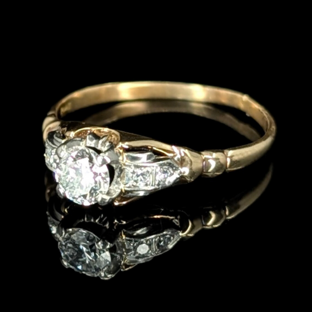 Art Deco gold ring with a sparkling 1/2 carat center diamond and two accent diamonds on each shoulder, reflecting on a black background.
