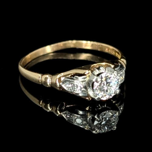 Art Deco gold ring with a sparkling 0.5 carat center diamond and two accent diamonds on each shoulder, reflecting on a black background.