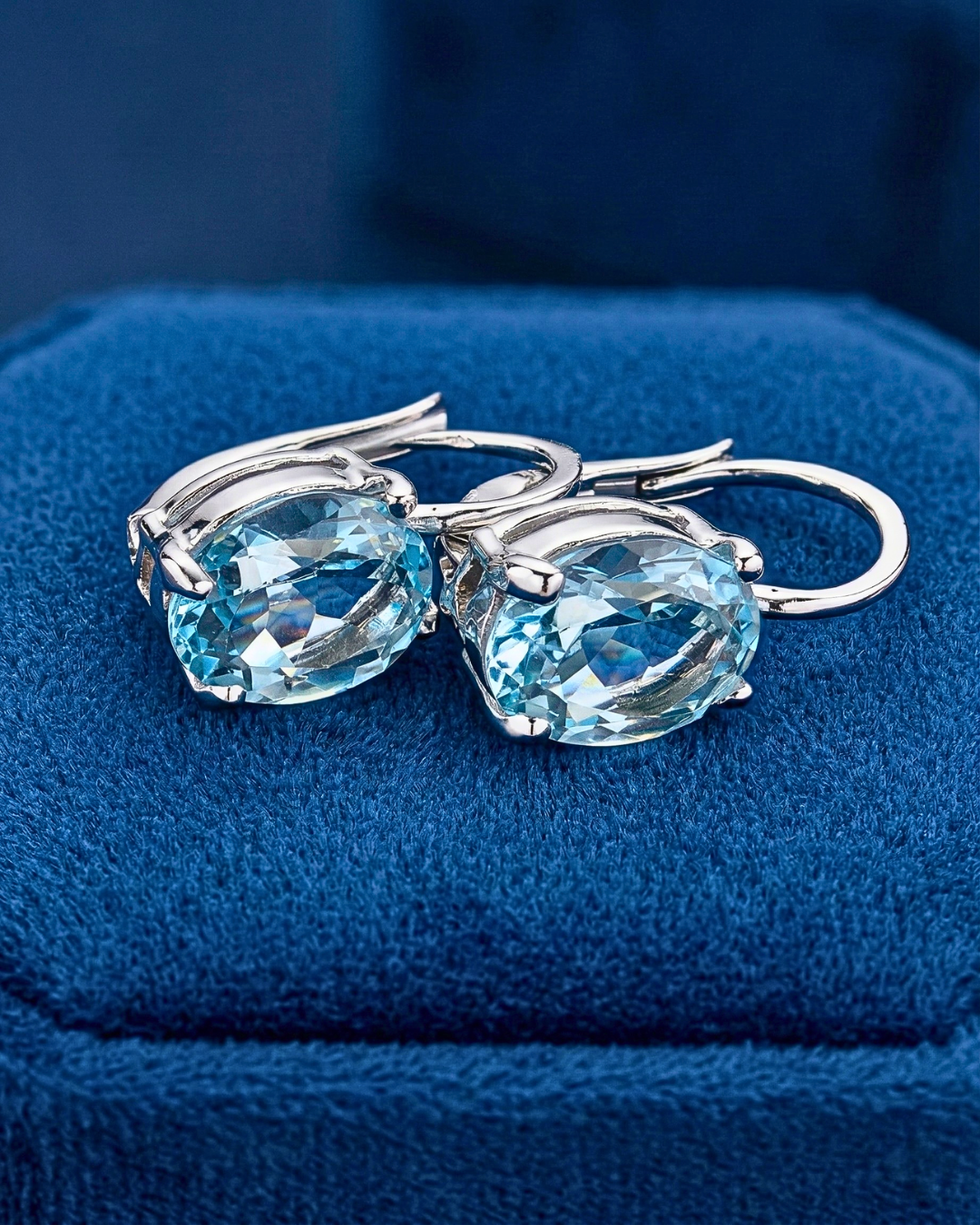 Pair of silver earrings with blue gemstones on a blue textured surface