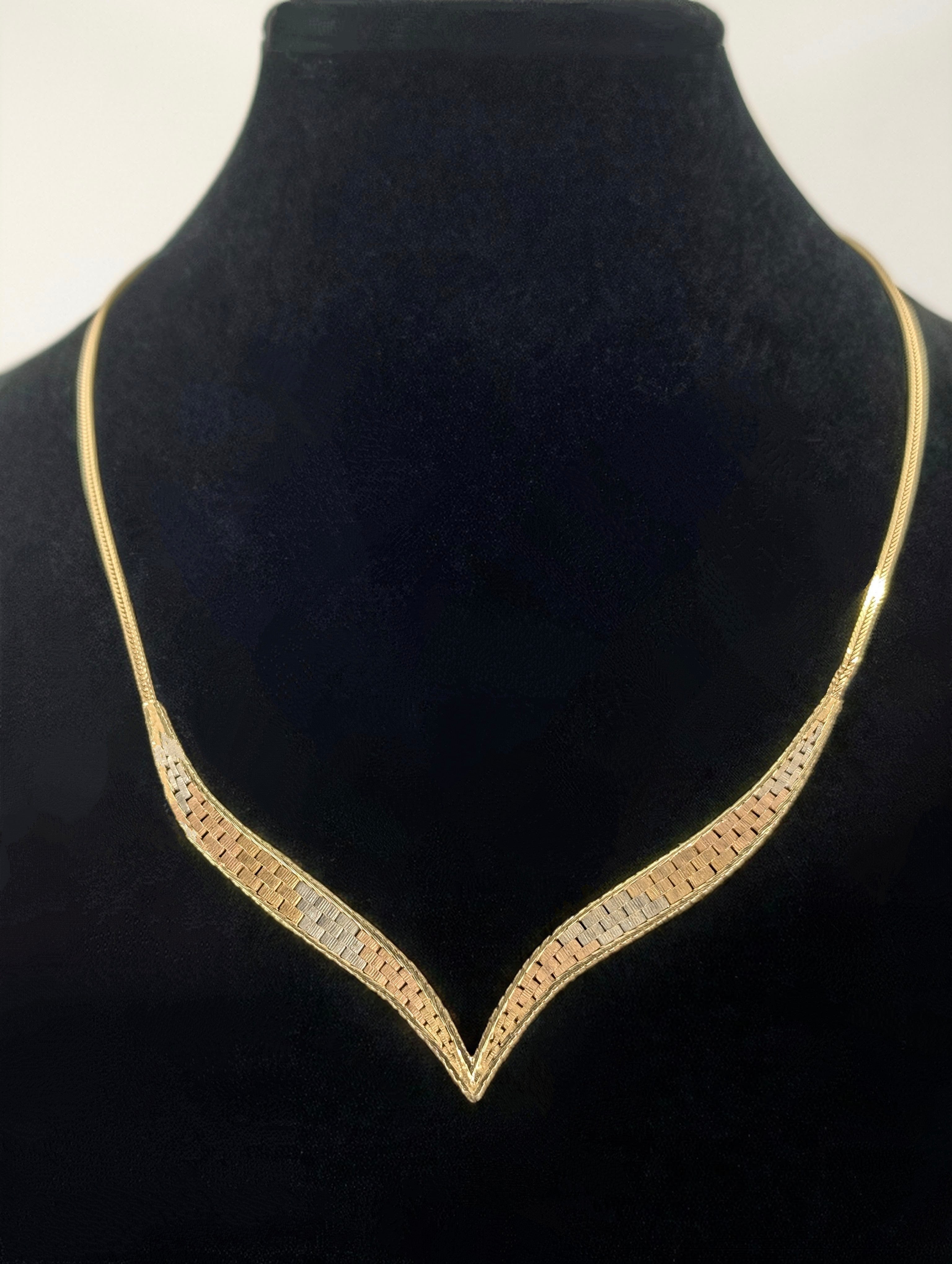 A tri-color gold V-shaped necklace featuring a central chevron design with yellow, white, and rose gold flat links, displayed on a black neck form.