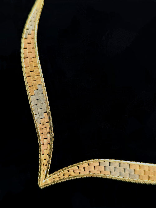 A tri-color gold V-shaped necklace featuring a central chevron design with yellow, white, and rose gold flat links, displayed on a black neck form.