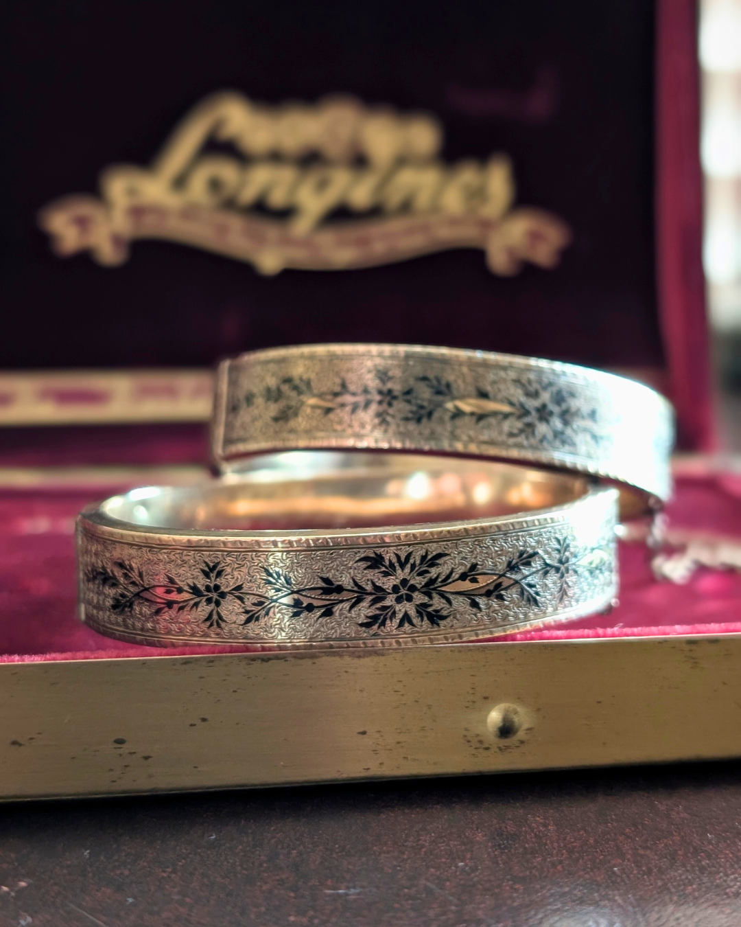 Children's Victorian gold hinged bangles with taille d’épargne black tracery enamel and an 1875 engraved inscription, displayed in a burgundy jewelry box.
