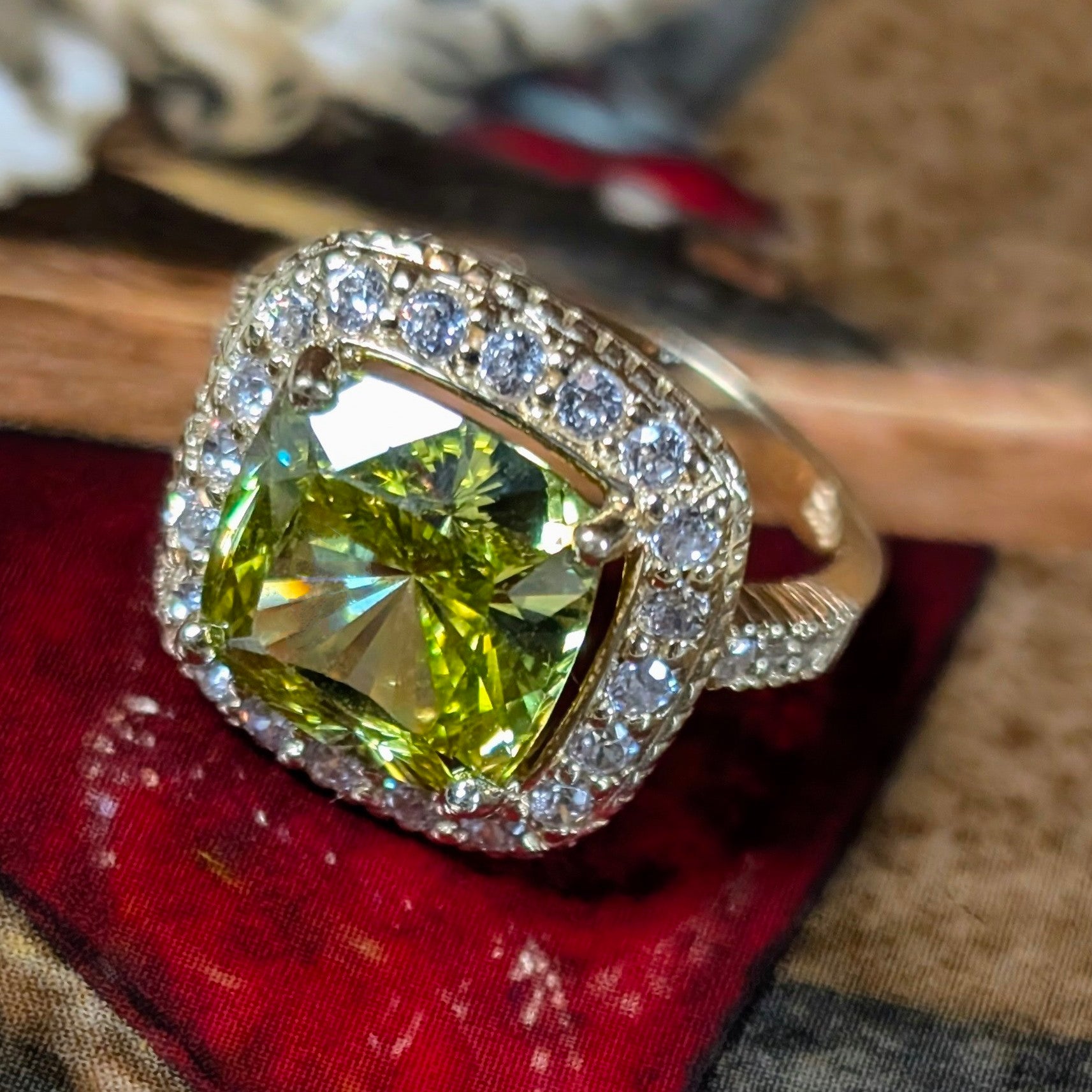 14K yellow gold ring featuring a large cushion-cut green peridot surrounded by a sparkling halo, on a red colorful decorative dish.